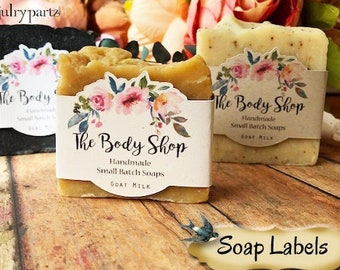 Peut inclure: Trois savons avec des étiquettes indiquant "The Body Shop" et "Handmade Small Batch Soaps Goat Milk". Les étiquettes présentent un motif floral avec des fleurs roses et bleues. Les savons sont posés sur une surface en bois. Le texte "Soap Labels" est sur une étiquette brune avec une bordure décorative.