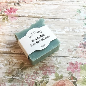 Puede incluir: Una barra cuadrada de jab&oacute;n azul claro con una etiqueta blanca que dice "Soul Feather Naturally Made Soaps, Bars and Lotions Studio".