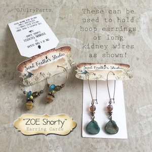 May include: Two earring display cards with the text "Soul Feather Studio" and "ZOE Shorty" Earring Cards. The cards are decorated with a nature-inspired design. The first card shows two hoop earrings with brown and green beads. The second card shows two long earrings with turquoise stones and brown beads.