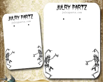 May include: Two white card stock earring display cards with black skeletons dancing on each card. The cards have the text "Julry Partz" and "julrypartz.com" printed on them. The text "Dancing Skeletons" is printed below the cards.