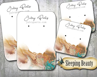 Peut inclure: Cartes d'affichage de boucles d'oreilles blanches avec un motif aquarelle dans les tons or, cuivre et sarcelle. Les cartes portent l'inscription "Julry Partz" et "julrypartz.com". Les mots "Sleeping Beauty" sont également visibles.