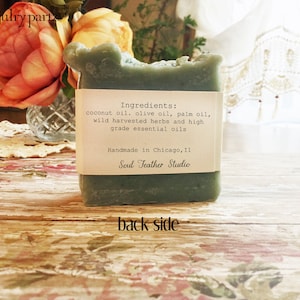 Puede incluir: Una barra de jab&oacute;n verde con una etiqueta blanca que dice "Ingredientes: aceite de coco, aceite de oliva, aceite de palma, hierbas silvestres cosechadas y aceites esenciales de alta calidad. Hecho a mano en Chicago, IL Soul Feather Studio."