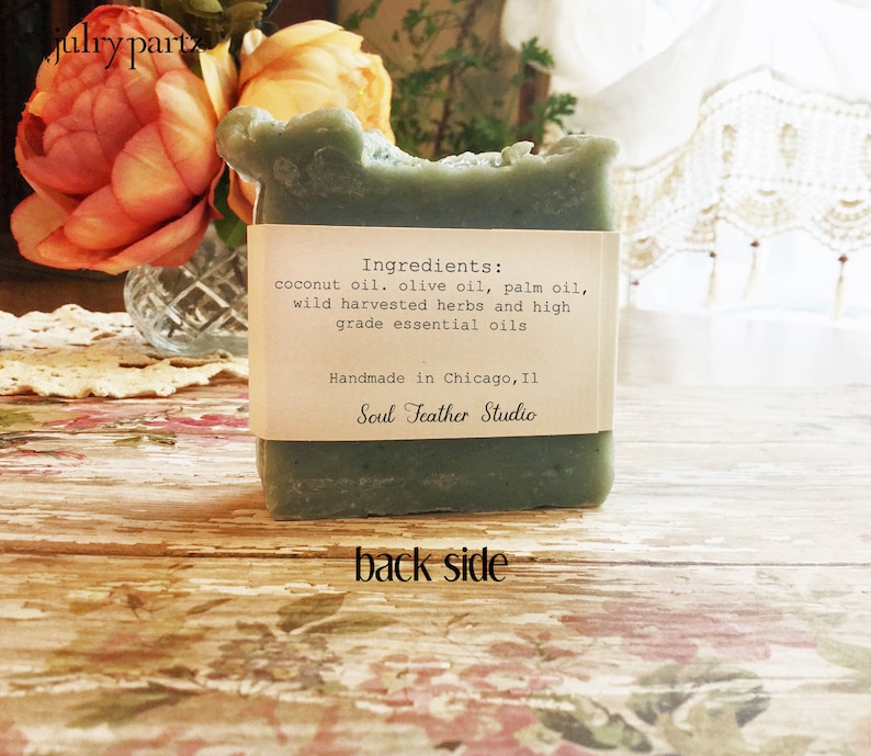 Puede incluir: Una barra de jab&oacute;n verde con una etiqueta blanca que dice "Ingredientes: aceite de coco, aceite de oliva, aceite de palma, hierbas silvestres cosechadas y aceites esenciales de alta calidad. Hecho a mano en Chicago, IL Soul Feather Studio."
