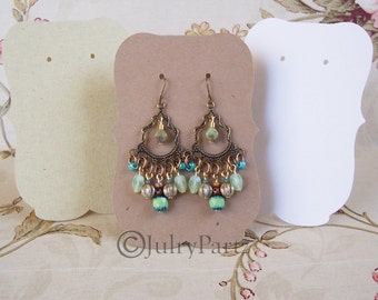 Peut inclure: Une paire de boucles d'oreilles pendantes avec une monture en métal doré et des perles de verre vertes et bleues. Les boucles d'oreilles sont présentées sur une carte brune avec le texte "Julkry Parts" imprimé dessus.