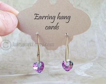 Peut inclure: Une paire de boucles d'oreilles créoles dorées avec un pendentif en cristal en forme de cœur violet. Les boucles d'oreilles sont suspendues à une carte brune sur laquelle est inscrit "Earring hang cards".