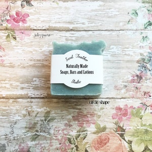 Puede incluir: Una barra de jab&oacute;n verde azulado con una etiqueta blanca que dice "Soul Teather Naturally Made Soaps, Bars and Lotions Studio" sobre un fondo con estampado floral.