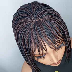 May include: A braided wig with a bob style. The wig features a mix of black and brown braids, creating a two-tone effect. The braids are neatly arranged, and the wig is styled on a mannequin head.