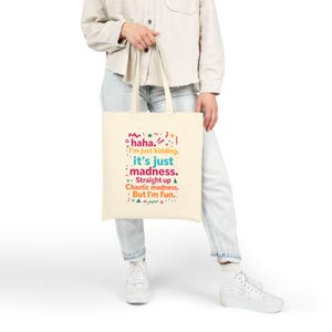 May include: A cream-colored tote bag with the text "haha. I'm just kidding. it's just madness. Straight up Chaotic madness. But I'm fun." in colorful lettering. The bag is held by a person.