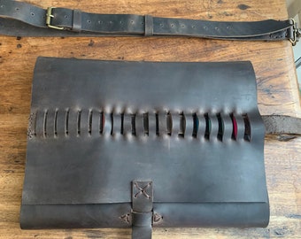 May include: A brown leather roll-up case with a strap and a buckle. The case has multiple slots for holding items, and the slots are visible through the stitching.