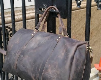 May include: A dark brown leather duffel bag with brass hardware hanging on a black metal gate.