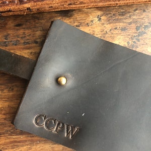 Op de afbeelding: Een donkerbruine leren sleutelhanger met een messing klinknagel en de initialen CCPW gegraveerd in het leer.