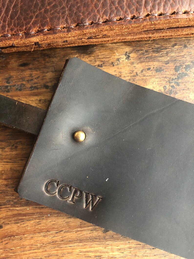 Op de afbeelding: Een donkerbruine leren sleutelhanger met een messing klinknagel en de initialen CCPW gegraveerd in het leer.