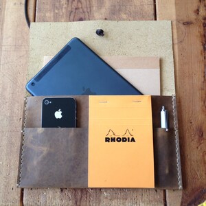 May include: A brown leather portfolio with a black tablet, a black smartphone, a pen, and a yellow notepad with the text "RHODIA" on it.