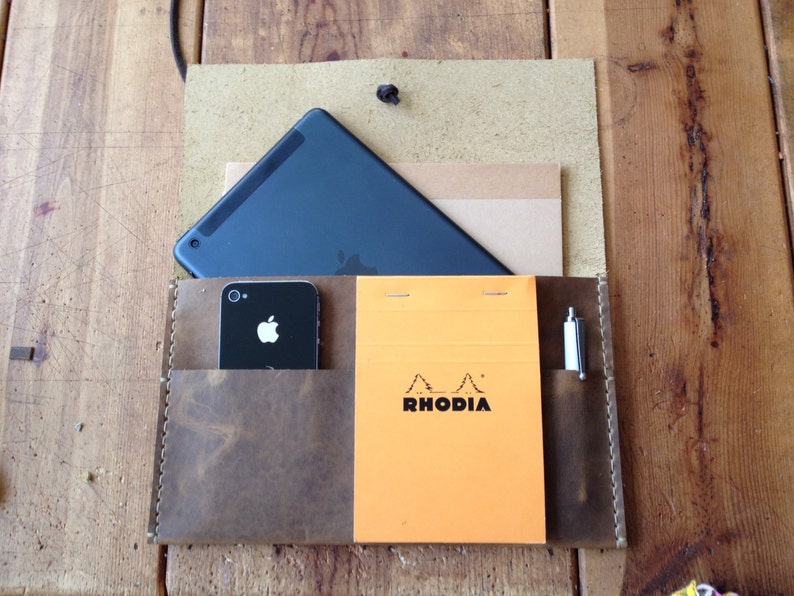 May include: A brown leather portfolio with a black tablet, a black smartphone, a pen, and a yellow notepad with the text "RHODIA" on it.