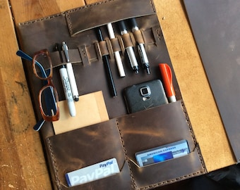 May include: A brown leather portfolio with multiple pockets and slots for holding pens, a phone, and cards. The portfolio has a PayPal and American Express card in the pockets.