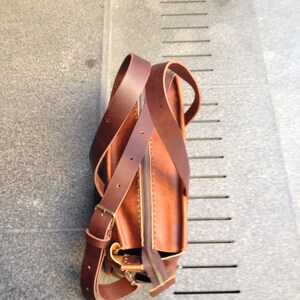 May include: A brown leather satchel bag with a long strap. The bag has a zipper closure and a flap with a buckle.