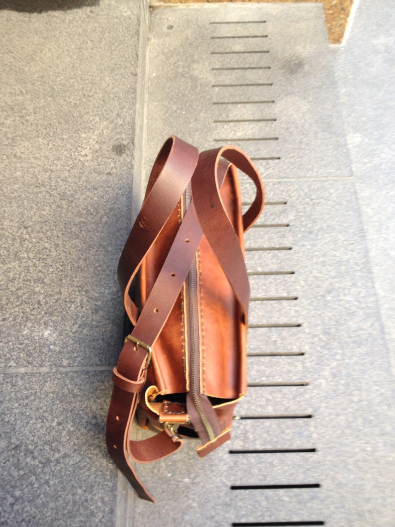 May include: A brown leather satchel bag with a long strap. The bag has a zipper closure and a flap with a buckle.