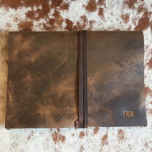 May include: A brown leather journal with a strap closure and the initials "DJP" embossed on the cover.