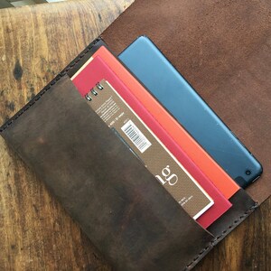 May include: A dark brown leather case, open to reveal a blue tablet, and several art pads in red, orange, and brown. The case is made of distressed leather and has visible stitching.