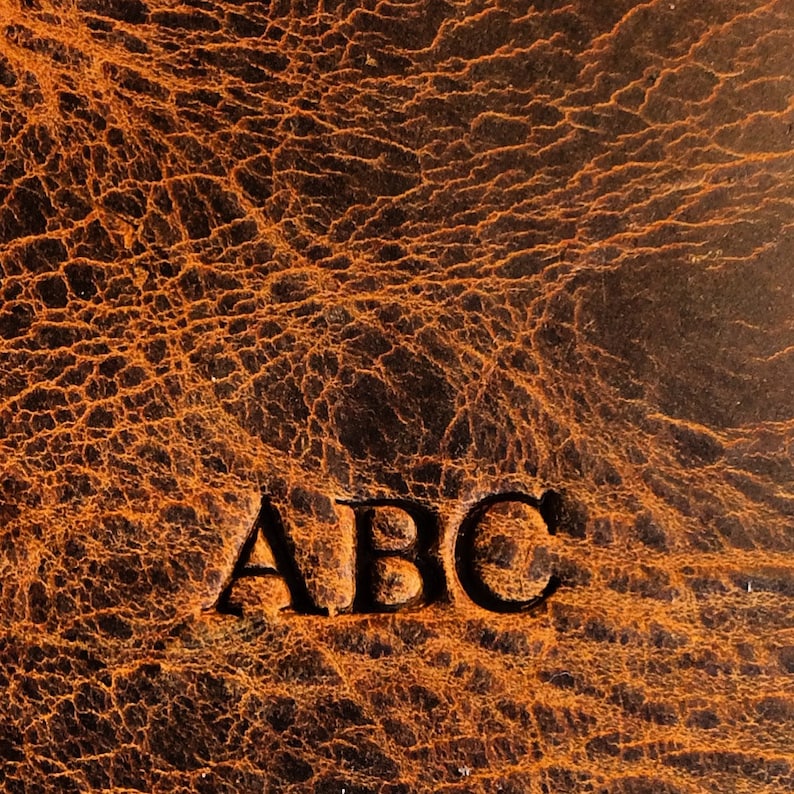 Op de afbeelding: Close-up van een bruin lederen oppervlak met de letters "ABC" in zwart reli&euml;f.