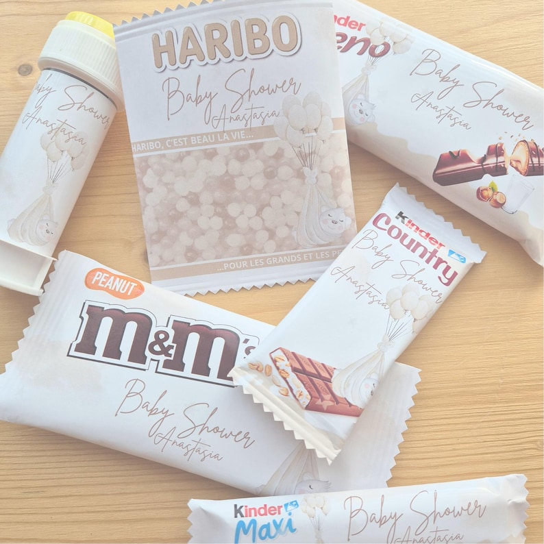 May include: Assortment of baby shower treats, including a Haribo candy bag, M&M's, and Kinder chocolate bars. The packaging is white with gold lettering and features baby-themed illustrations and the name "Anastasia."