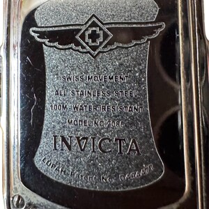 May include: Close-up of the back of an Invicta watch. The watch is stainless steel and water-resistant to 100 meters. The text on the watch reads "SWISS MOVEMENT", "ALL STAINLESS STEEL", "MODEL NO 2085", and "INVICTA".