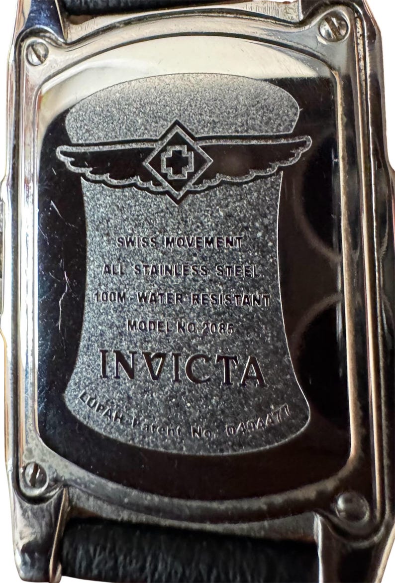 May include: Close-up of the back of an Invicta watch. The watch is stainless steel and water-resistant to 100 meters. The text on the watch reads "SWISS MOVEMENT", "ALL STAINLESS STEEL", "MODEL NO 2085", and "INVICTA".