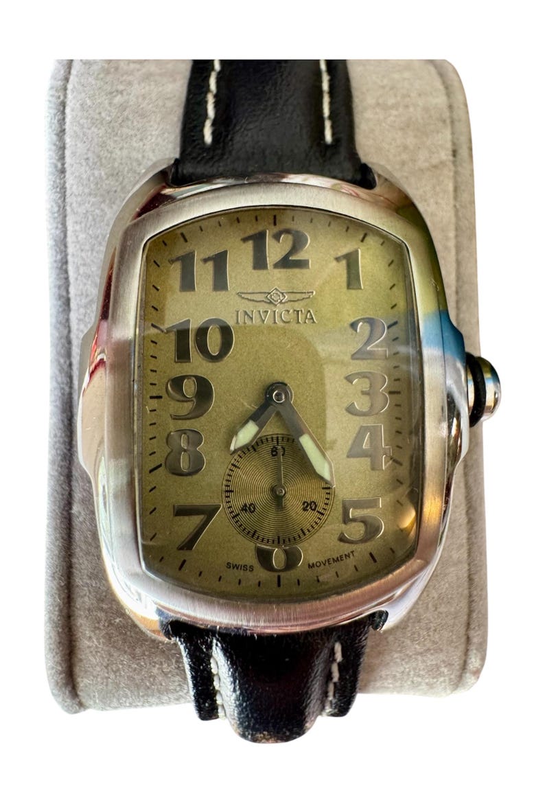 May include: A silver-toned Invicta watch with a rectangular face and a black leather band. The watch face is a light olive green with large black numerals and a small subdial. The watch is marked "SWISS MOVEMENT".