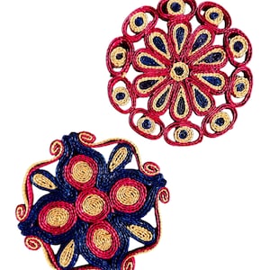 May include: Two decorative coasters with floral designs. The coasters are made of woven material in red, blue, and gold colors. The coasters have a circular and a square shape.