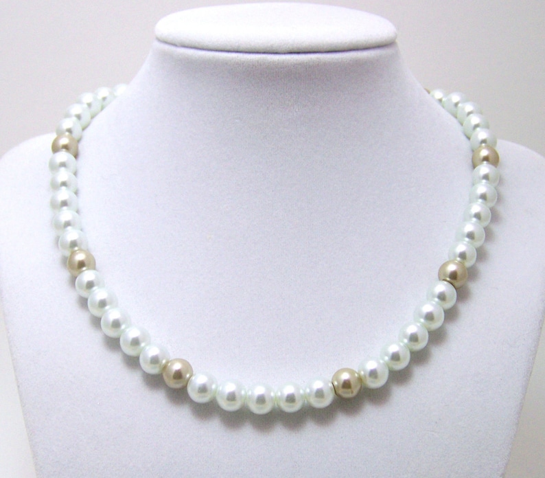 May include: A white pearl necklace with gold accents. The necklace is on a white mannequin bust.