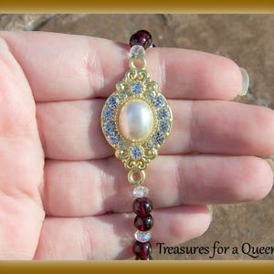 May include: A gold-tone bracelet with a large, oval-shaped pearl surrounded by clear rhinestones. The bracelet is made of small, red and clear beads.