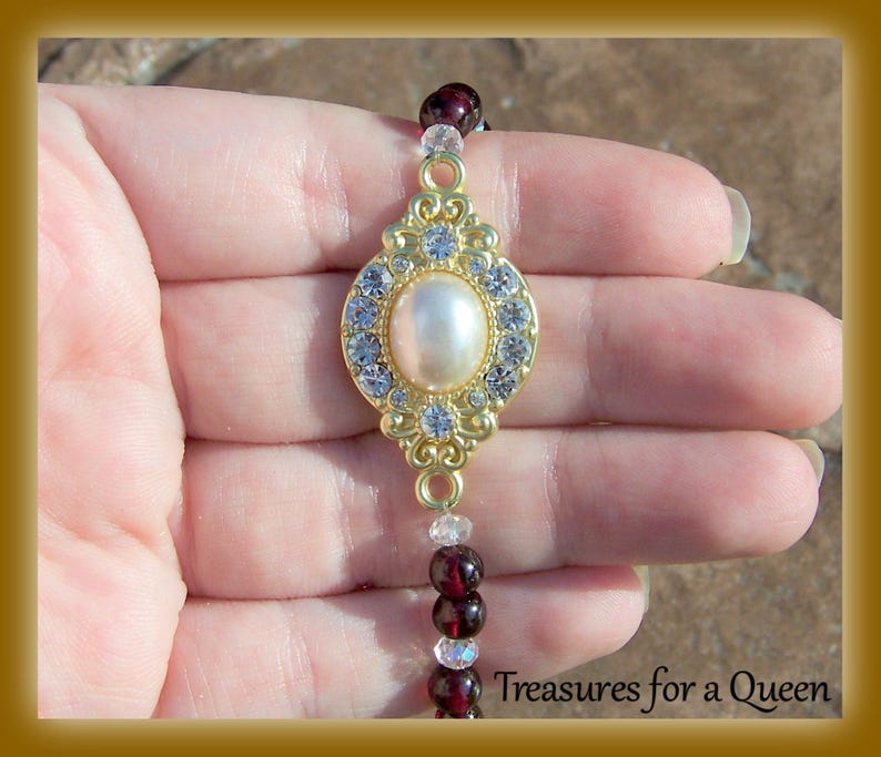 May include: A gold-tone bracelet with a large, oval-shaped pearl surrounded by clear rhinestones. The bracelet is made of small, red and clear beads.