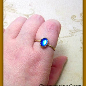 Puede incluir: Un anillo de oro con una piedra ovalada azul engastada en un engaste de oro. La piedra tiene un acabado ligeramente iridiscente.