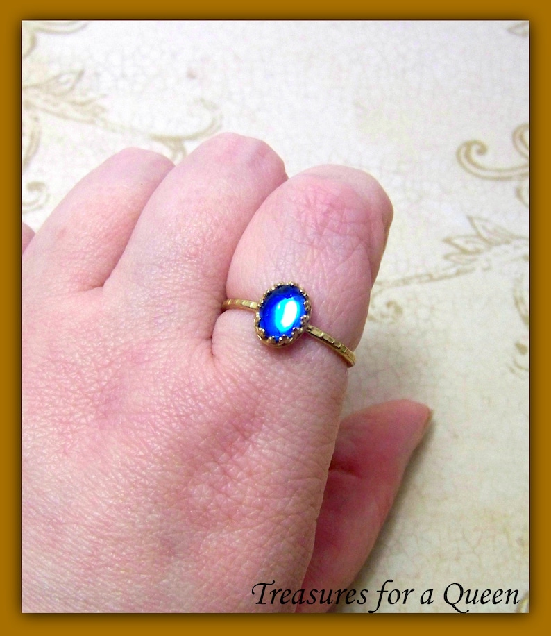 Puede incluir: Un anillo de oro con una piedra ovalada azul engastada en un engaste de oro. La piedra tiene un acabado ligeramente iridiscente.