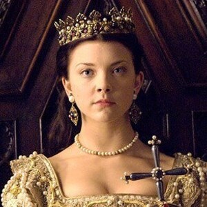 May include: A woman wearing a gold crown with red and white gems, a pearl necklace, and pearl earrings. She is holding a silver cross with pearl accents. She is wearing a gold and white dress.