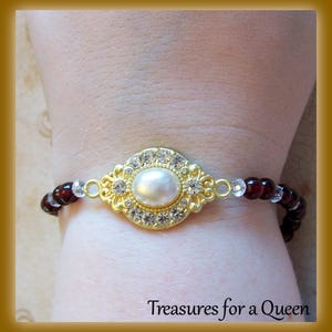 May include: A gold bracelet with a large pearl surrounded by clear rhinestones. The bracelet is made of small red and clear beads.