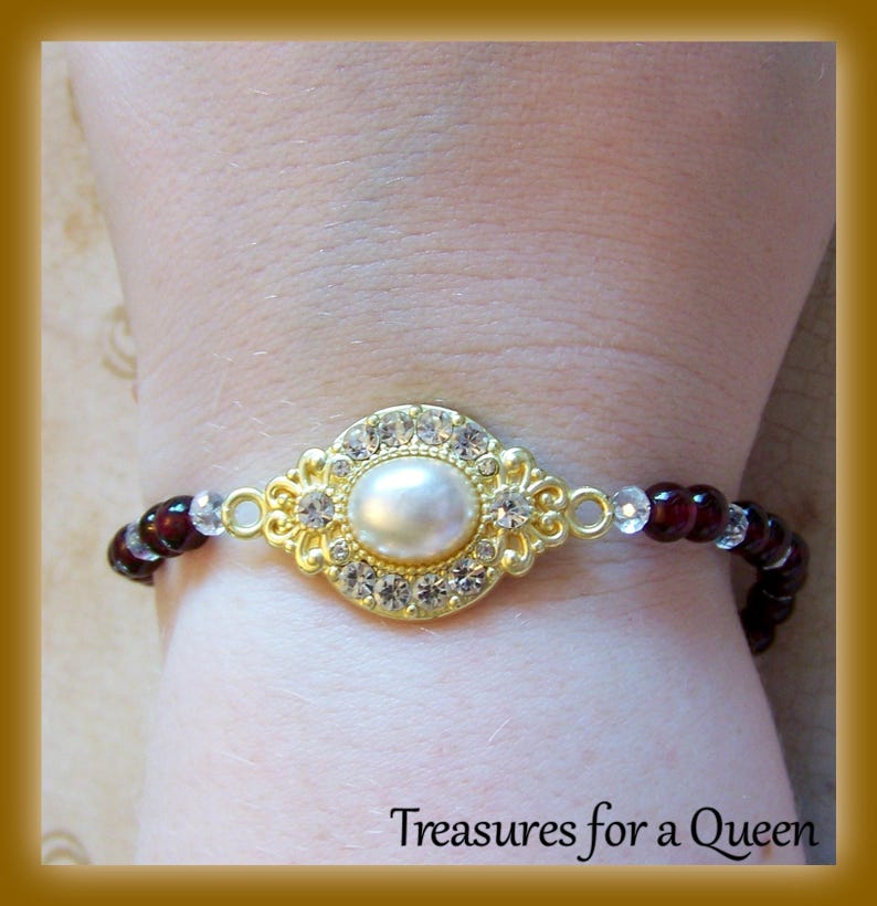 May include: A gold bracelet with a large pearl surrounded by clear rhinestones. The bracelet is made of small red and clear beads.