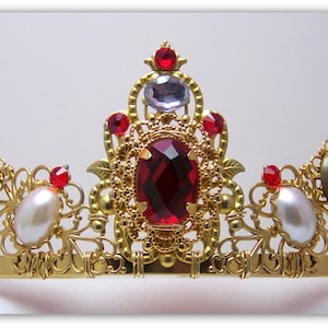 Puede incluir: Una corona dorada con piedras preciosas rojas y blancas, perlas y detalles filigranados intrincados.