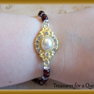 May include: A gold bracelet with a large pearl and clear rhinestones. The bracelet is made of small red and clear beads.