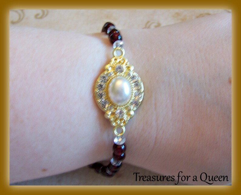 May include: A gold bracelet with a large pearl and clear rhinestones. The bracelet is made of small red and clear beads.
