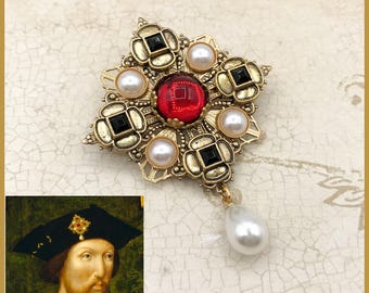 May include: A gold-tone brooch with a red jewel in the center, surrounded by black and white faux pearls. The brooch has a dangling pearl drop.