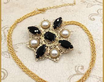 May include: A gold chain necklace with a black and white pendant. The pendant is a starburst design with black gemstones and white pearls.