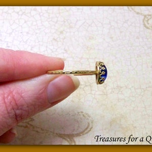 Puede incluir: Un anillo de oro con una piedra de vidrio azul engastada en un bisel con forma de corona. El anillo est&aacute; en un dedo.