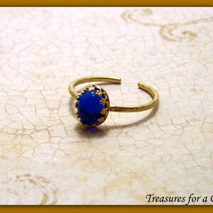 Puede incluir: Un anillo de oro con una piedra preciosa ovalada azul engastada en un engaste de filigrana de oro.