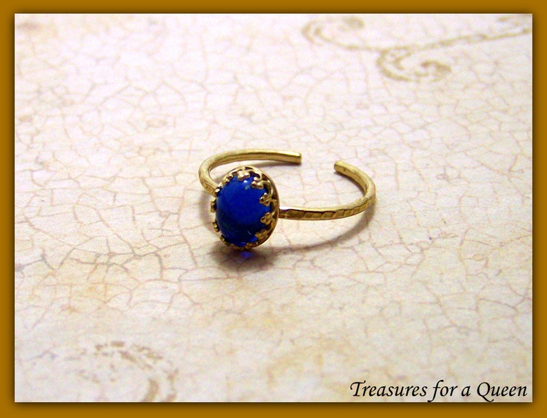 Puede incluir: Un anillo de oro con una piedra preciosa ovalada azul engastada en un engaste de filigrana de oro.