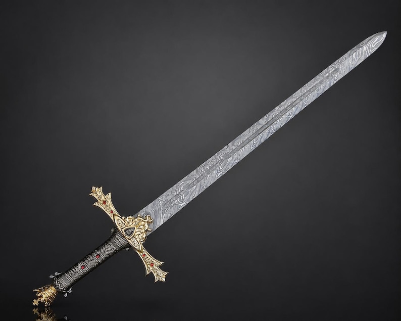 May include: A long sword featuring a silver-toned blade with a distinct wavy Damascus steel pattern. The hilt is crafted with ornate gold-colored metal accents, including a lion head motif, and is inlaid with small red stones along the crossguard.