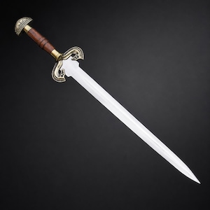 May include: A double-edged sword featuring a polished steel blade, a dark brown wooden handle, and an ornate brass-toned crossguard. The pommel is rounded and decorated with intricate metal engravings, matching the style of the crossguard.