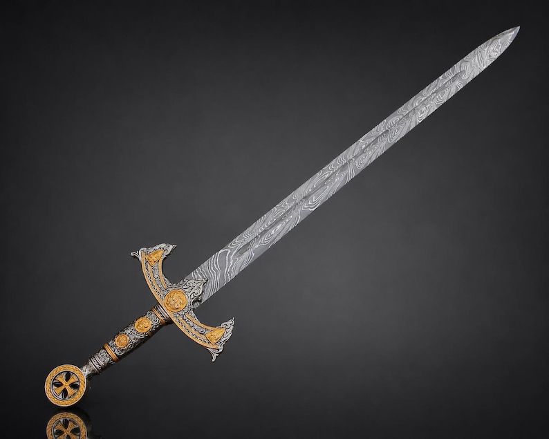 May include: A long sword featuring a Damascus steel blade with a distinct wavy pattern. The hilt is crafted from silver-toned metal with gold-colored accents, including a circular pommel with a cross design and a crossguard with ornate detailing.