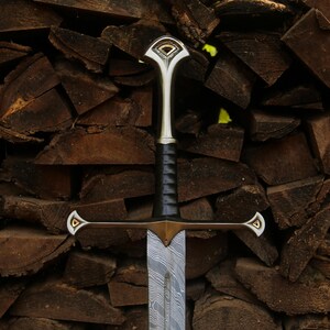 May include: A sword featuring a patterned Damascus steel blade, a black leather-wrapped grip, and a metallic crossguard and pommel. The crossguard and pommel are accented with gold-colored triangular inlays at the tips and center.