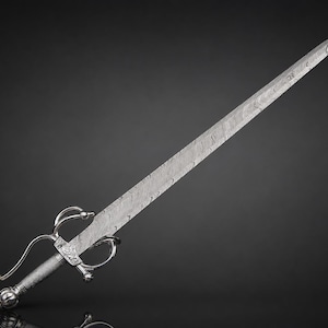 May include: A rapier with a long, pointed blade featuring a distinct wavy Damascus steel pattern. The hilt is constructed from polished silver-toned metal, showcasing a complex swept-hilt guard, a textured cylindrical grip, and a rounded pommel.
